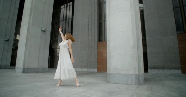 Young dancer in white dress dances in the gallery of columns architectural complex in slow motion, balerina does dance steps and pa outdoors, 4k 120 fps Prores HQ — Vídeo de stock