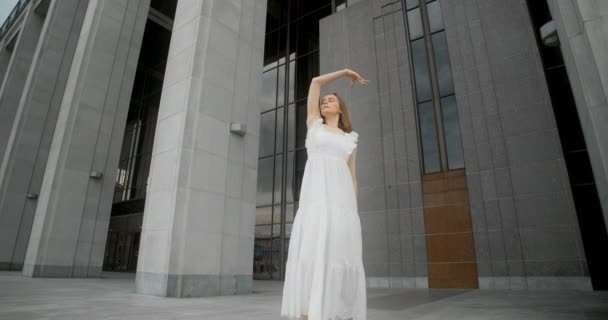 Young dancer in white dress dances in the gallery of columns architectural complex in slow motion, balerina does dance steps and pa outdoors, 4k 120 fps Prores HQ — Vídeo de stock