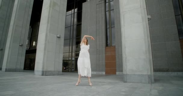 Young dancer in white dress dances in the gallery of columns architectural complex in slow motion, balerina does dance steps and pa outdoors, 4k 120 fps Prores HQ — Stock video