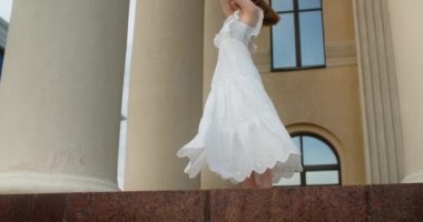 Young balerina in white dress whirls between the colums of the building in slow motion, balerina dances outdoors, 4k 120 fps Prores HQ