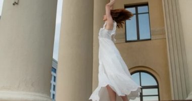 Young balerina in white dress whirls between the colums of the building in slow motion, balerina dances outdoors, 4k 120 fps Prores HQ