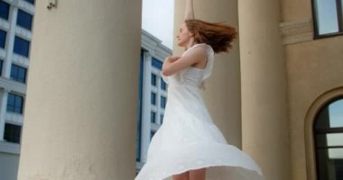 Young balerina in white dress whirls between the colums of the building in slow motion, balerina dances outdoors, 4k 120 fps Prores HQ