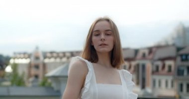 Portrait of the young european woman with nose earring in white dress in the city, she smiles, straightens her hair and looks at the camera, 4k Prores HQ
