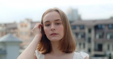 Portrait of the young european woman with nose earring in white dress in the city, she smiles, straightens her hair and looks at the camera, 4k Prores HQ