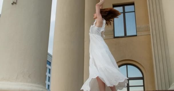 Young balerina in white dress whirls between the colums of the building in slow motion, balerina dances outdoors, 4k 120 fps Prores HQ — Vídeo de Stock