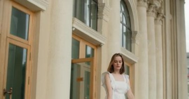 Young dancer woman in white dress whirls in the gallery of columns architectural complex in slow motion, balerina dances outdoors, 4k 120 fps Prores HQ