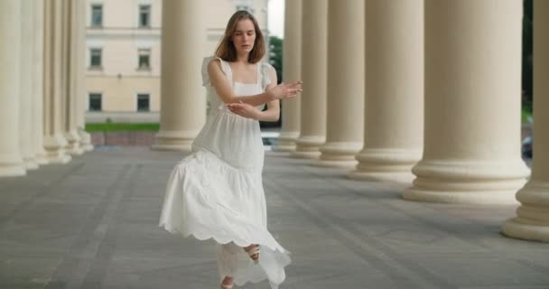 Young dancer woman in white dress whirls in the gallery of columns architectural complex in slow motion, balerina dances outdoors, 4k 120 fps Prores HQ — Stockvideo