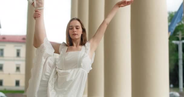 Young dancer woman in white dress whirls in the gallery of columns architectural complex in slow motion, balerina dances outdoors, 4k 120 fps Prores HQ — Wideo stockowe
