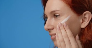 Portrait of pretty woman applying cream to her face. Womens cosmetics usage. Beauty care procedures on blue screen, 4k Prores HQ