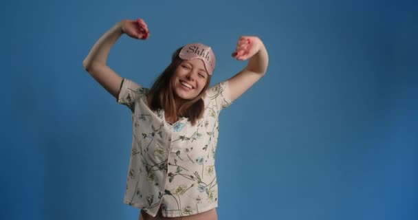 Portrait of a young woman in night sleeping mask smiling to the camera and stretching after sleep on the blue background, 4k 60p Prores HQ — Video