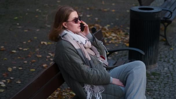 Woman have a talk by smartphone sitting on the bench in the street of old town, 4k 60p — Stockvideo