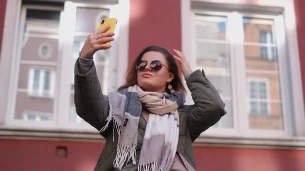 Жінка в сонцезахисних окулярах робить селфі на вулиці старого міста восени, 4k 60p повільний рух — стокове відео
