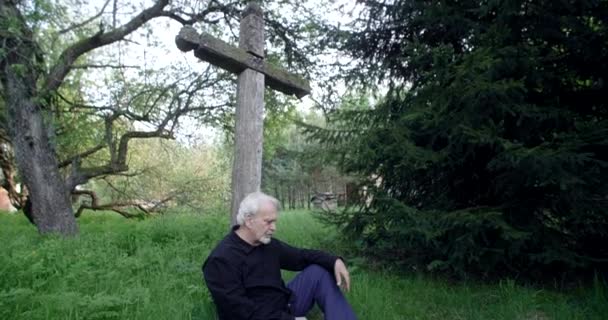 Triste vieil homme aux cheveux gris assis sur la tombe avec une grande vieille croix au cimetière, tristesse et tristesse à propos de la perte de personnes proches, 4k 60p Prores — Video
