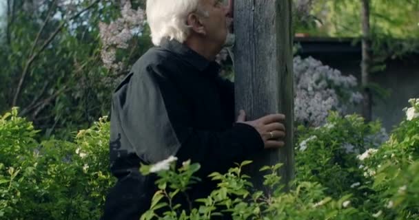 Üzgün, yaşlı, gri saçlı adam mezarlıkta büyük, ahşap bir haçın yanında duruyor. Yakın insanları kaybetmenin hüznü ve üzüntüsü. Dindar adam, 4k 60p Prores — Stok video