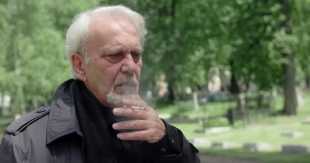 Sad old gray haired man smokes cigarette on the cemetery, sorrow and sadness about lost of close people, 4k 60p Prores — Stock Video