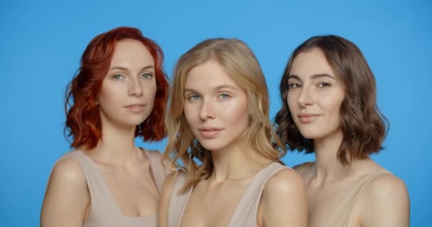 Bionda, rossa e donna dai capelli scuri stanno guardando e sorridendo alla fotocamera, ritratto di diversi tipi di donne sullo schermo blu, 4k 24p Prores — Video Stock