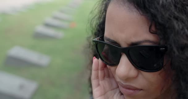 Potret wanita hitam yang sedang bersedih dengan kacamata hitam berdiri di atas kuburan. Pemakaman dan perpisahan, menghormati kerabat yang meninggal. 4k 60p Prores — Stok Video