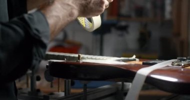 Luthier dükkanındaki perdeleri zımparalamadan önce gitar gövdesini maskeliyor. Müzikal enstrümanların bakım ve onarımı, 4k 60p Prores HQ