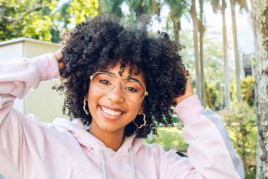 Afro saçlı, kıvırcık saçlı, gülümseyen ve kameraya bakan güzel Afro-Amerikan kadını.
