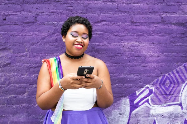 lgbt african american girl with cell phone chatting with lgbt flag in the city on purple wall background smiling