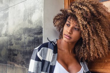 Kareli ceketli, kıvırcık saçlı, şehirdeki kafeye bakan güzel Afro-Amerikan kadının portresi..
