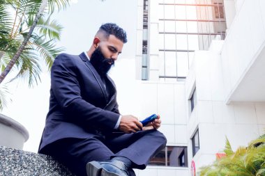 Successful business man with long beard wearing elegant suit and tie using his mobile outside corporate building in the city outdoors
