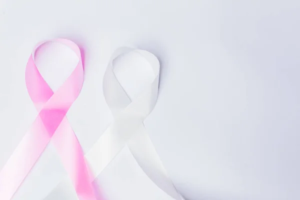 Pink ribbon fight against breast cancer and white ribbon to fight violence against women on isolated white background with space for text.