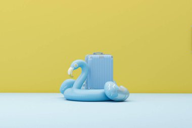 Blue Flamingo float, tropical bird shape inflatable swimming pool ring with luggage put on pastel blue and pink background. 3d rendering. Summer and travel minimal concept.