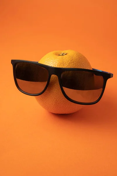 cool grapefruit with black plastic sun glass on bright orange background. minimal creative composition with copy space.