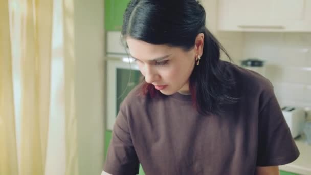 Молода біла жінка в коричневій футболці готує на домашній кухні — стокове відео