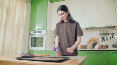 Genç beyaz kadın ev mutfağında hamurdan kurabiye kesiyor.