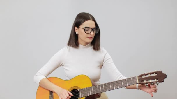 Mujer en traje beige afinando su guitarra acústica sobre un fondo gris — Vídeos de Stock