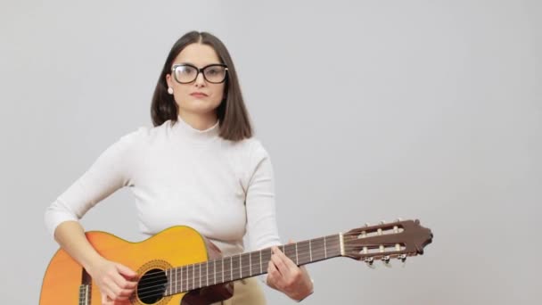 Kobieta w beżowym stroju gra akordy na akustycznej nylonowej gitarze — Wideo stockowe