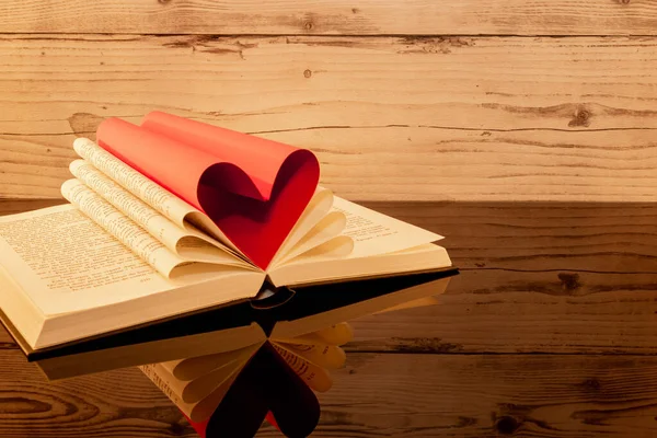 stock image Folded book in the shape of a heart on a wooden background.