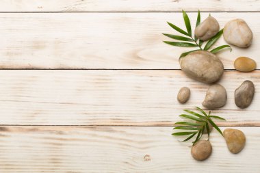 Tahta arka planda kaplıca taşları ve yapraklar, üst manzara.