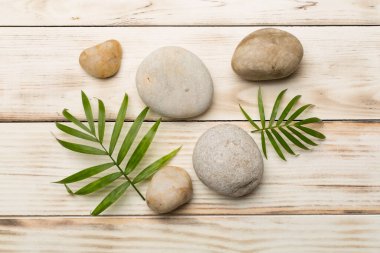 Tahta arka planda kaplıca taşları ve yapraklar, üst manzara.