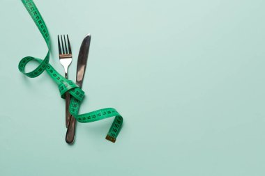 Renk arkaplanında çatal bıçak takımı olan yeşil mezura, üst görünüm.