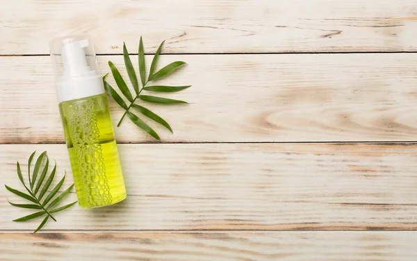 Foaming facial cleanser and cotton pads on wooden background, top view.