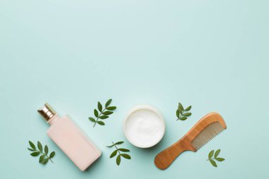 Shampoo and mask with herbal extract and comb on color background, top view.