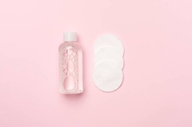 Renk arkaplanına Micellar temizleme suyu ve pamuk pedleri, üst görünüm.