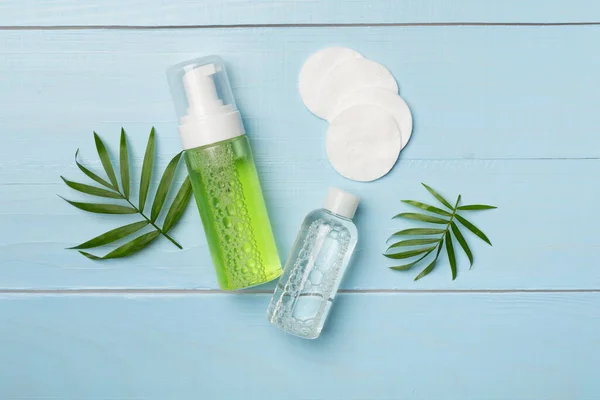 Foaming facial cleanser and micellar water on wooden background, top view.