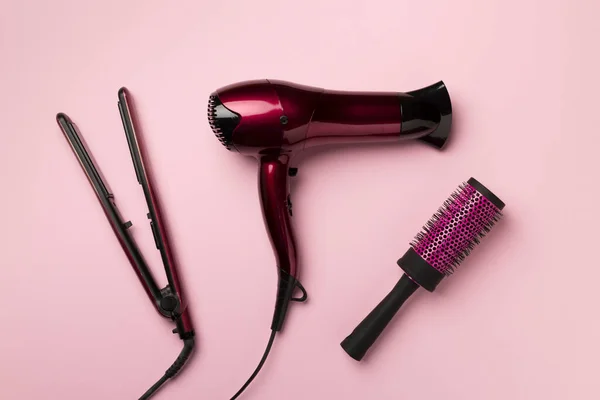 Hair dryer, straightener and brush on color background, top view.