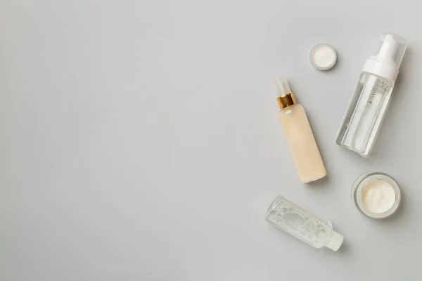 Different cosmetic bottles on color background, top view.