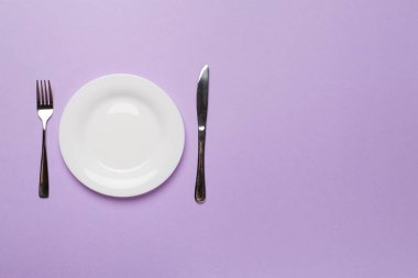 Empty dish with knife and fork on color background, top view.