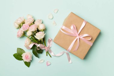 Gift box and rose flowers on color background, top view