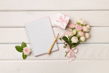 Notebook, gift box and rose flowers on wooden background, top view.