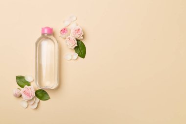 Micellar water with rose flower on color background, top view.