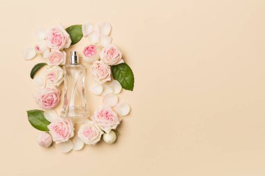 Bottle of perfume with rose flowers on color background, top view.