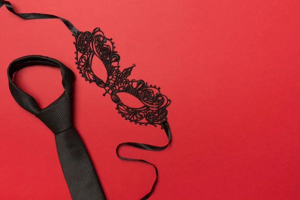 Lace mask and tie on color background, top view.
