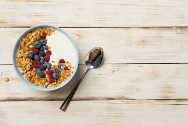 Bowl with granola, yogurt and fresh berries on wooden background, top view.
